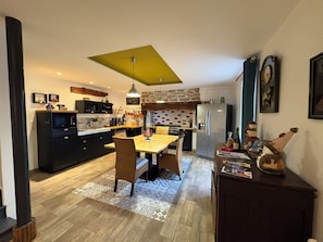 A modern kitchen with a dining area, featuring a large island, built-in appliances, and a unique ceiling design. - Detached house (Douarnenez)