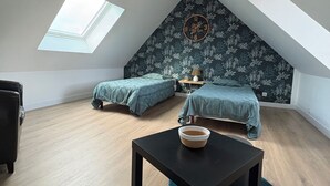 Een slaapkamer in loftstijl met dakraam, twee bedden, een rond poef en een kleine tafel.