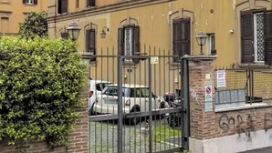Un edificio de varios pisos con fachada amarilla, entrada protegida por una verja y coches estacionados.