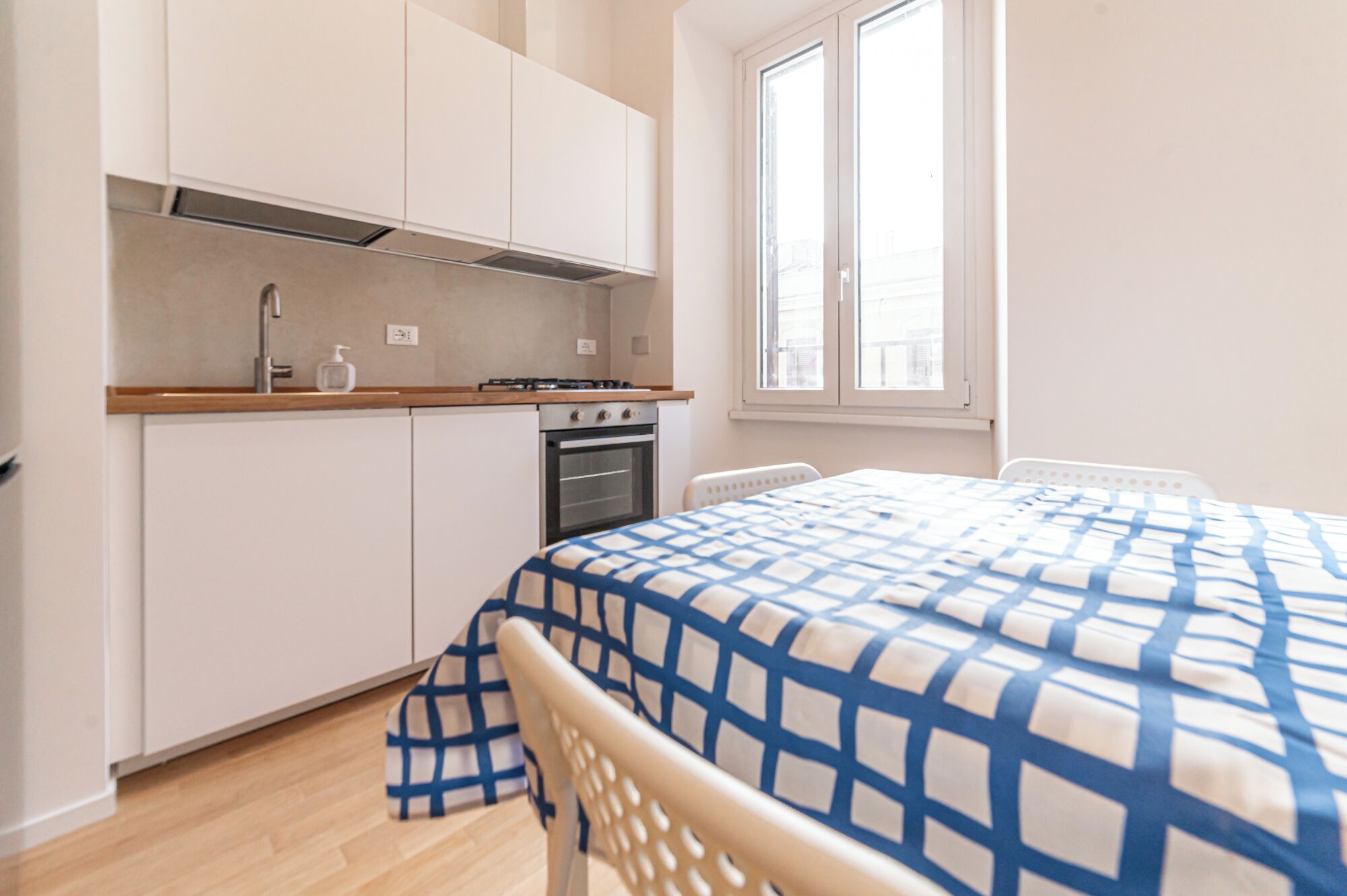 Une petite cuisine équipée d’une cuisinière, d’un four et d’un évier, un lit recouvert d’une couverture à carreaux et une fenêtre offrant une belle vue.