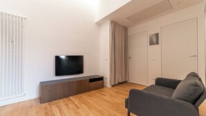 Una sala de estar moderna con una televisión de pantalla plana, piso de madera, un sofá gris y una puerta cerrada con un marco de fotos.