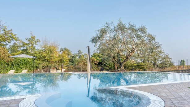 Une piscine avec une terrasse carrelée, des chaises longues et une pergola.