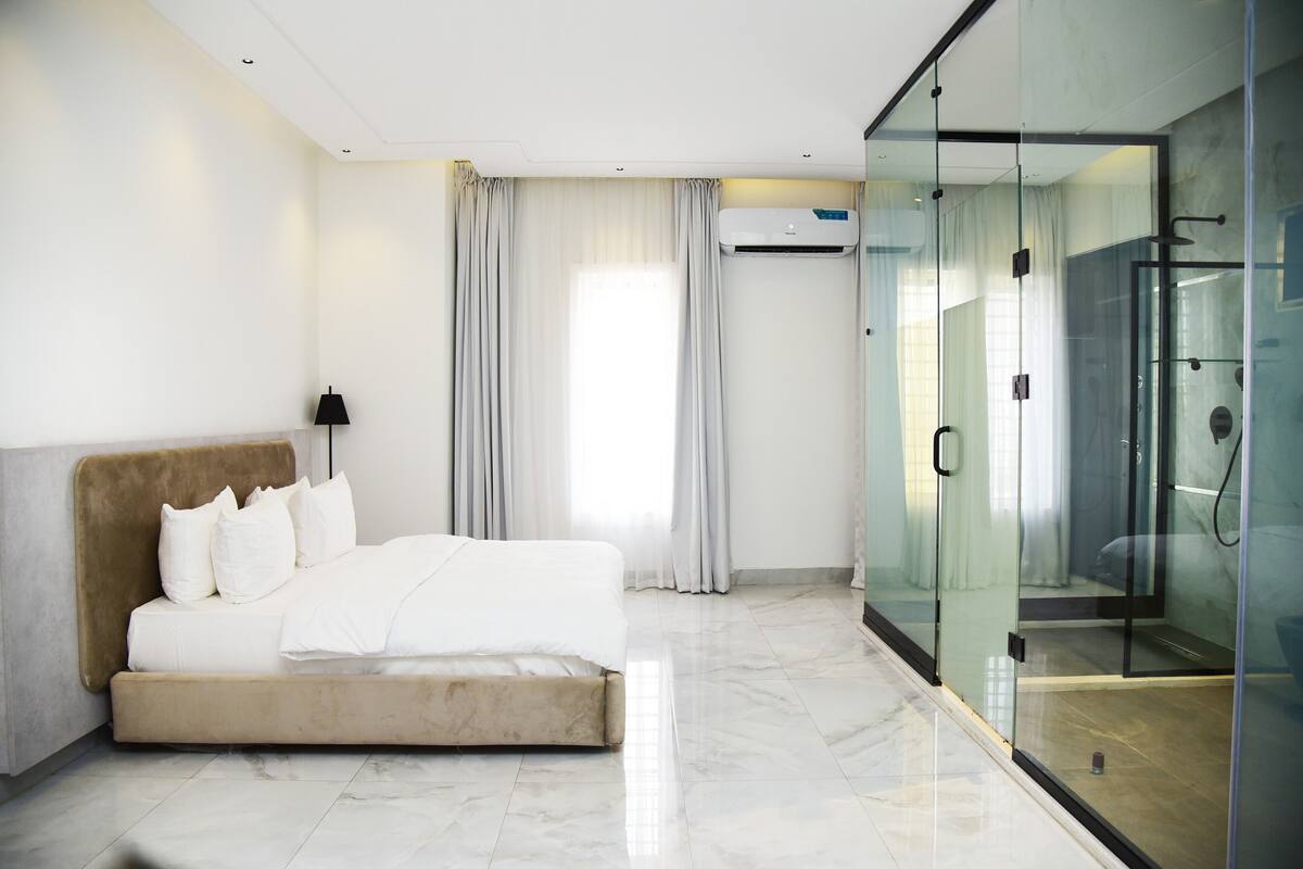 Une chambre d’hôtel moderne avec un lit, une douche en verre et une grande fenêtre avec des rideaux.
