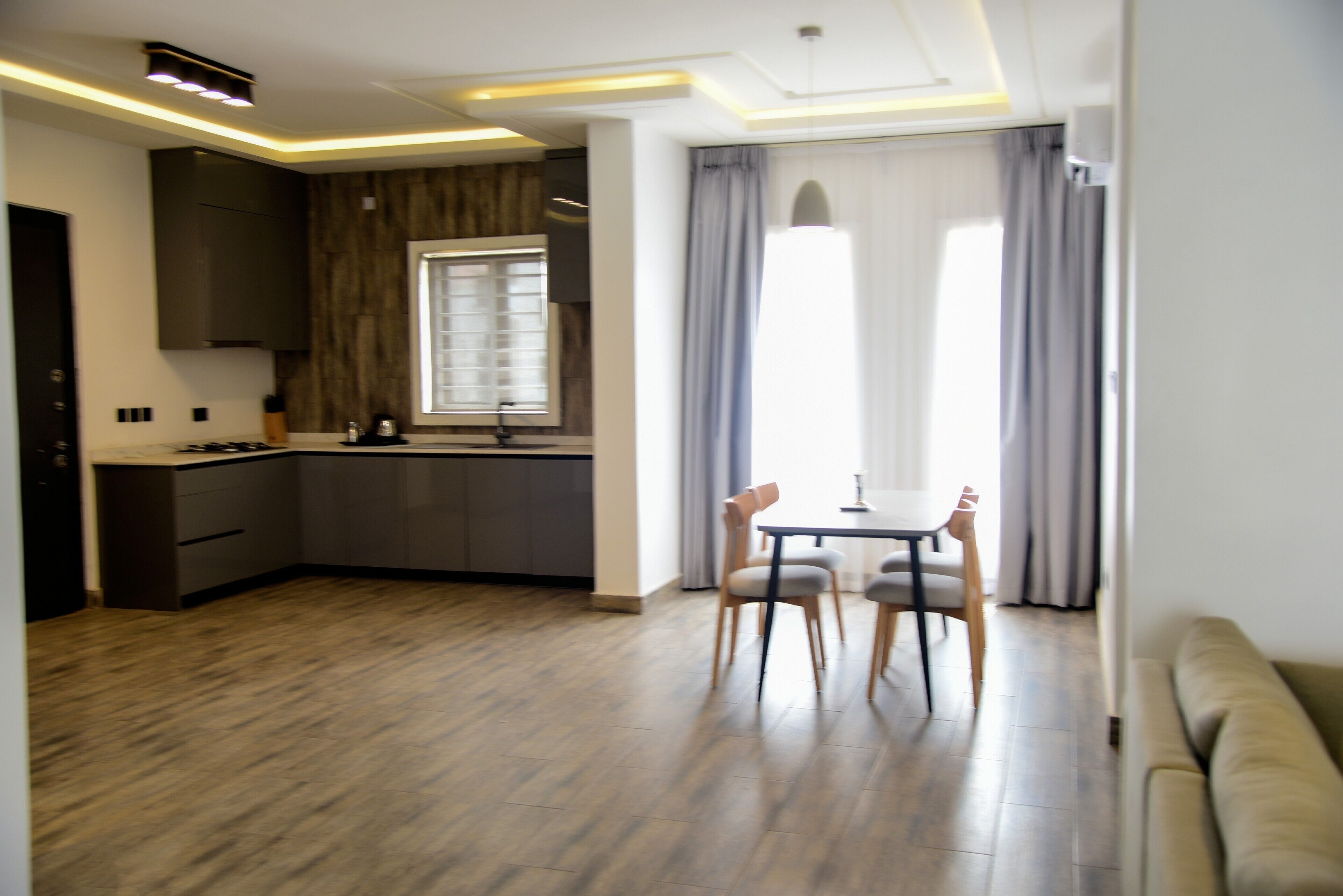 Eine moderne Küche mit eingebauten Geräten, ein Essbereich mit Tisch und Stühlen sowie ein großes Fenster mit Vorhängen.