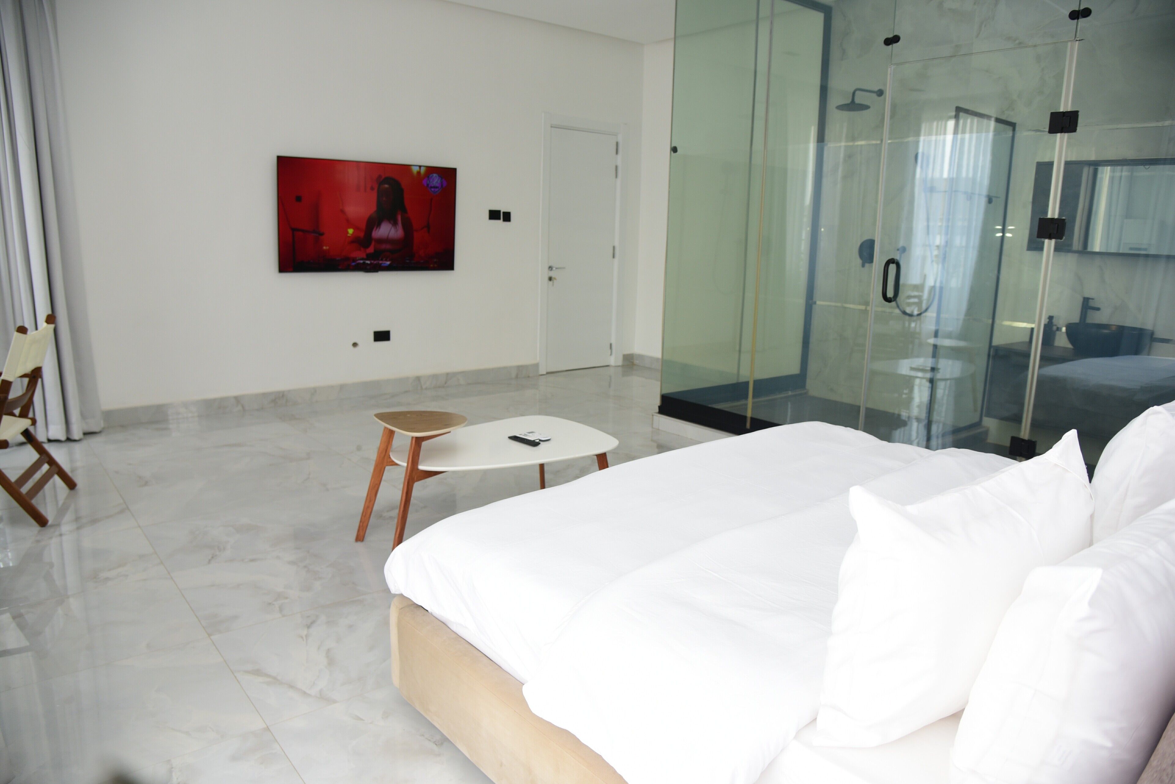 Een moderne hotelkamer met een groot bed, een kleintje tafeltje, een douche met glazen wand, een bevestigde televisie en een deur.