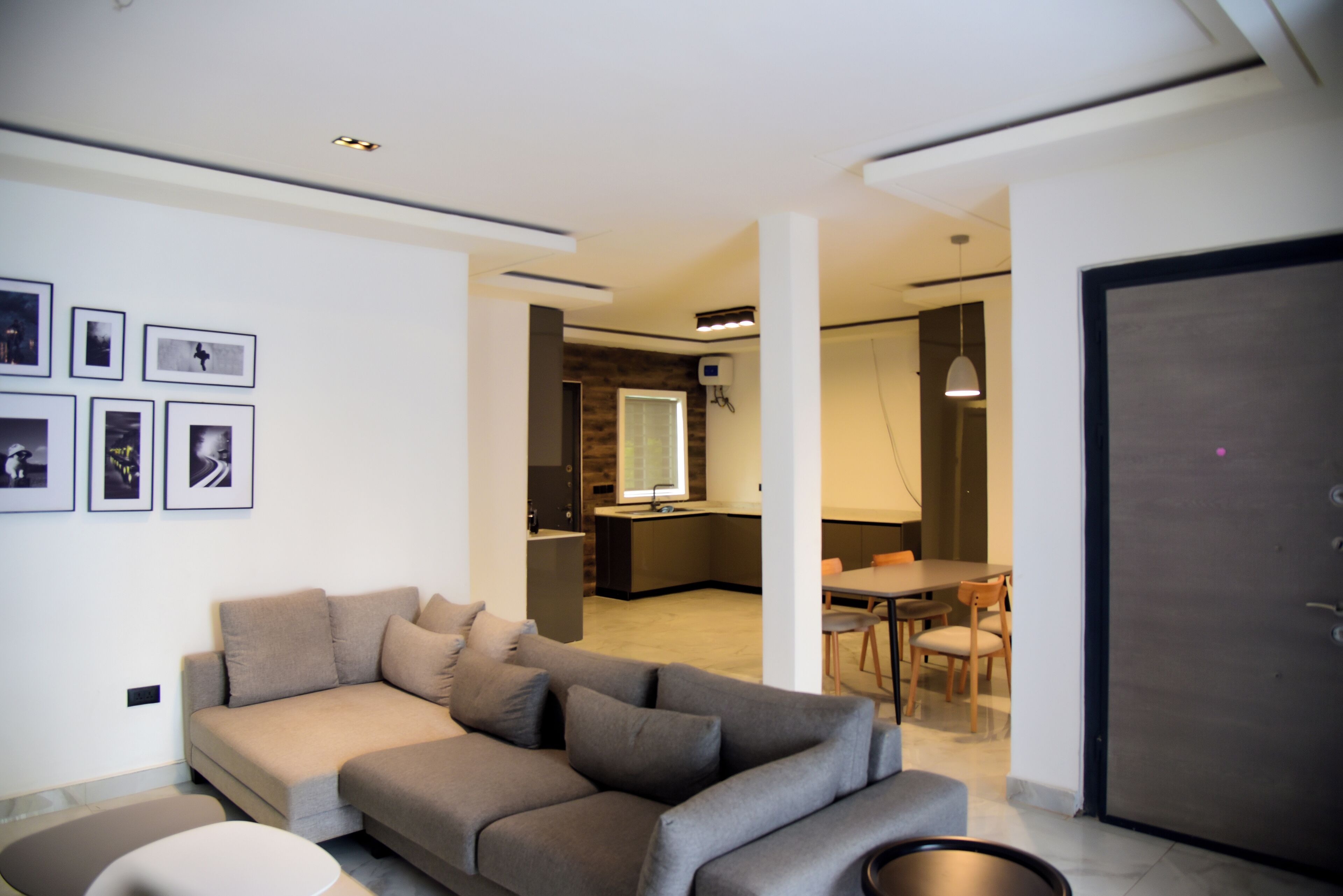 A modern living room with a sofa, a dining area with a table and chairs, and a kitchen in the background.