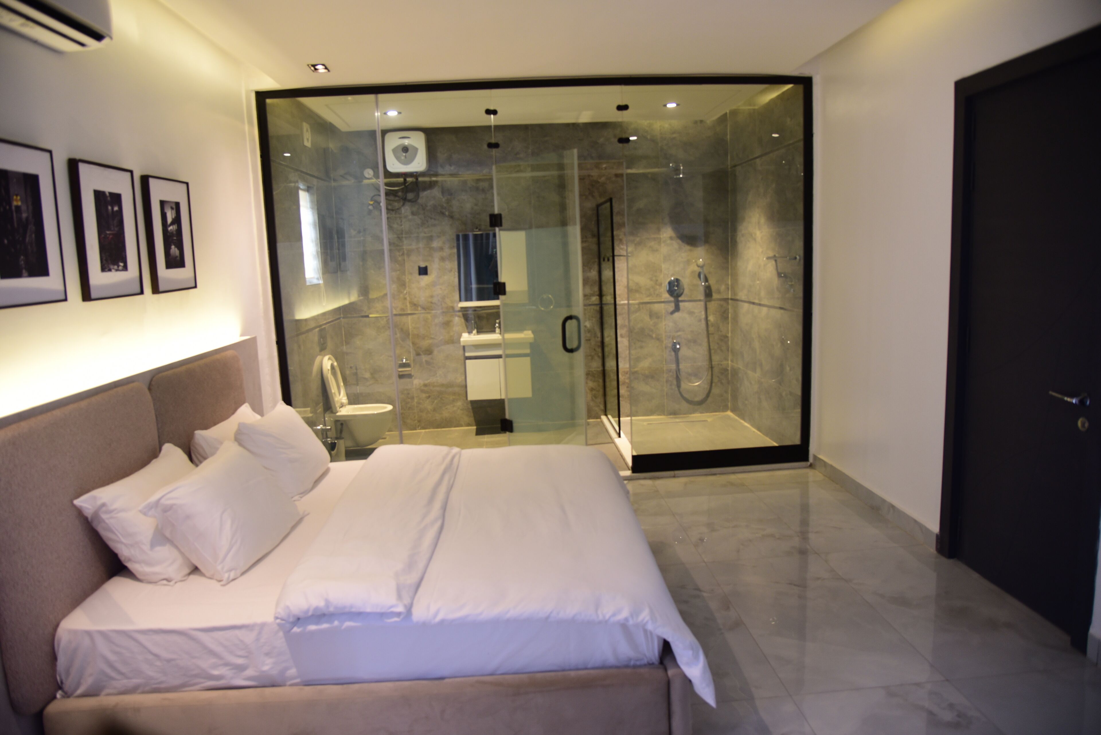A modern bedroom with a large bed, a glass-enclosed shower, and a dark door.