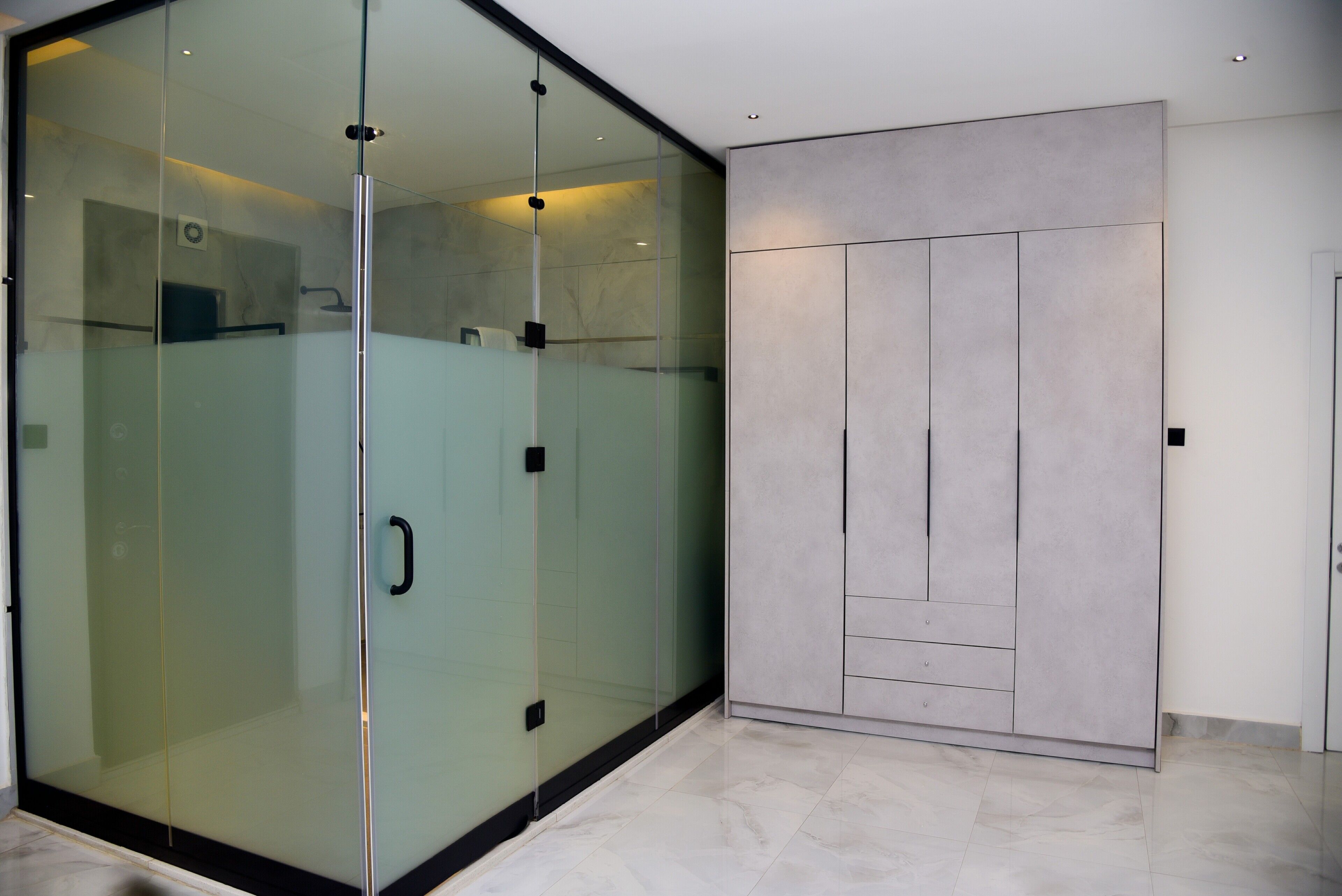 A modern room with a sliding glass door leading to a shower area, a built-in wardrobe with multiple compartments, and a tiled floor.