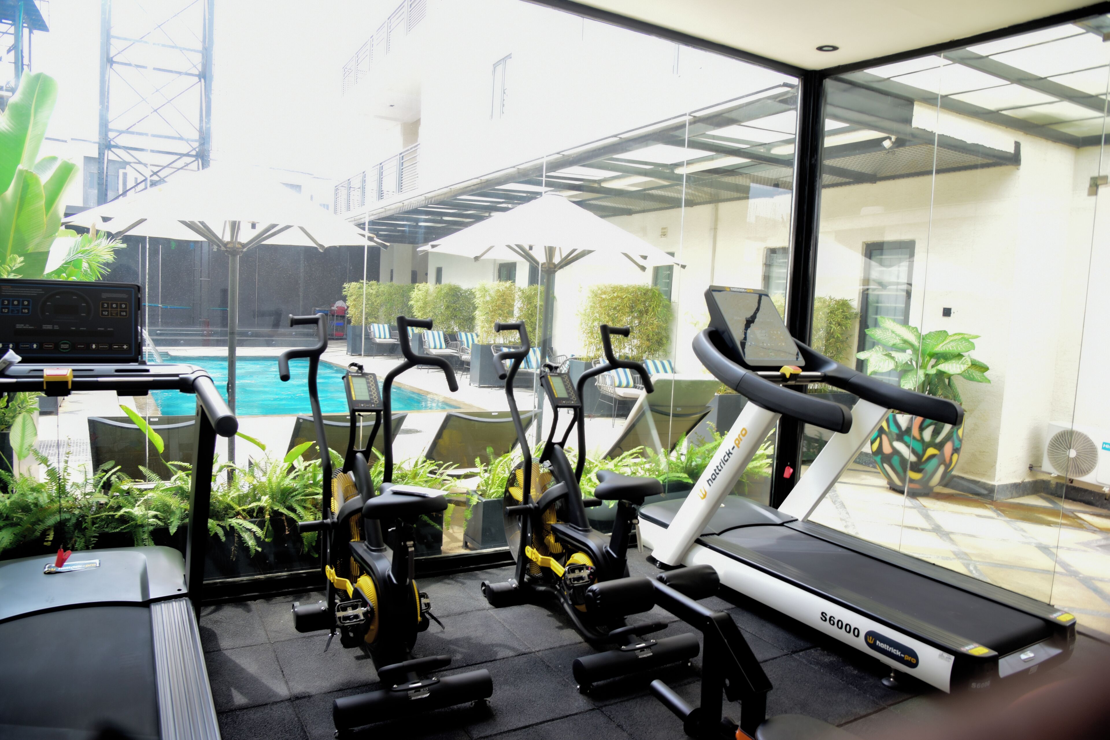 A gym with treadmills, elliptical machines, and a stationary bike, overlooking a swimming pool and outdoor seating area.