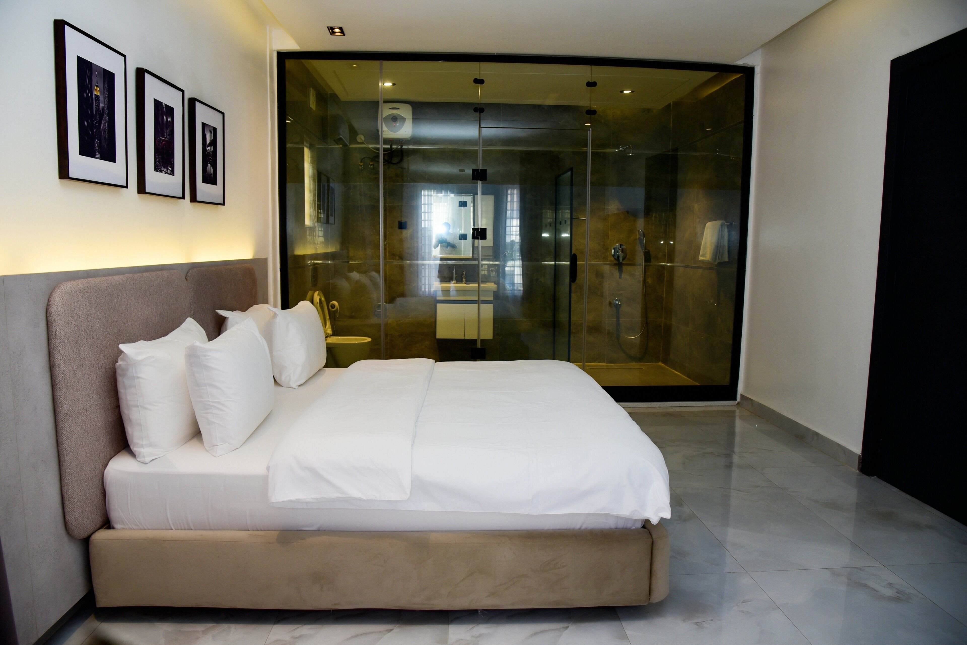 A modern bedroom with a large bed, a glass-enclosed shower, and framed pictures on the wall.
