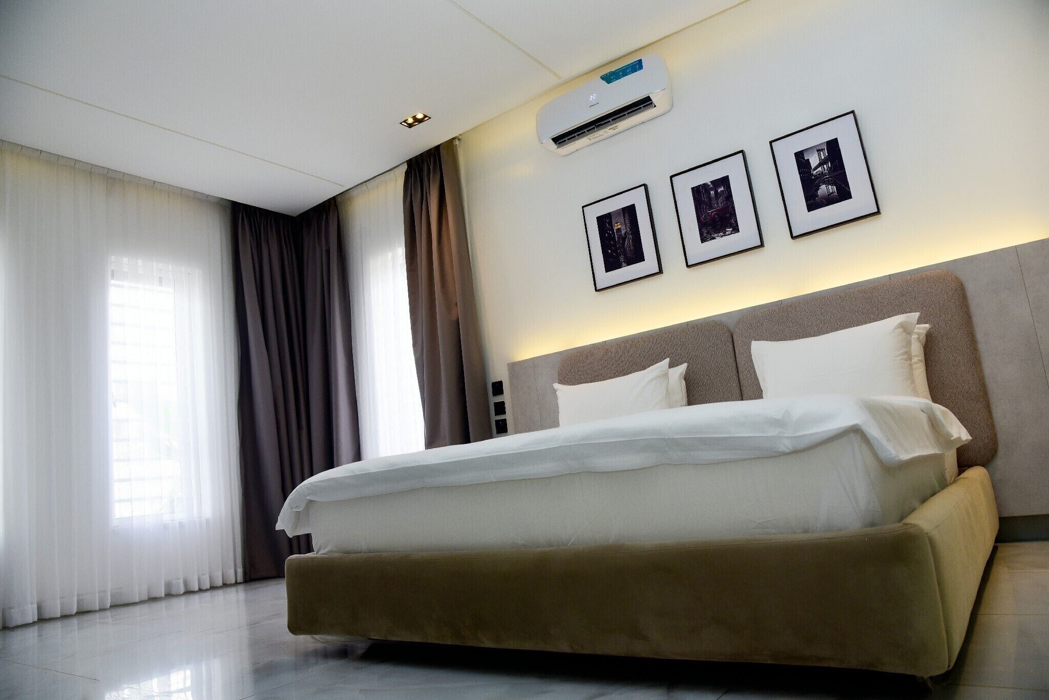 Una habitación de hotel con una cama grande, cabecera, aire acondicionado montado en la pared y tres cuadros enmarcados.