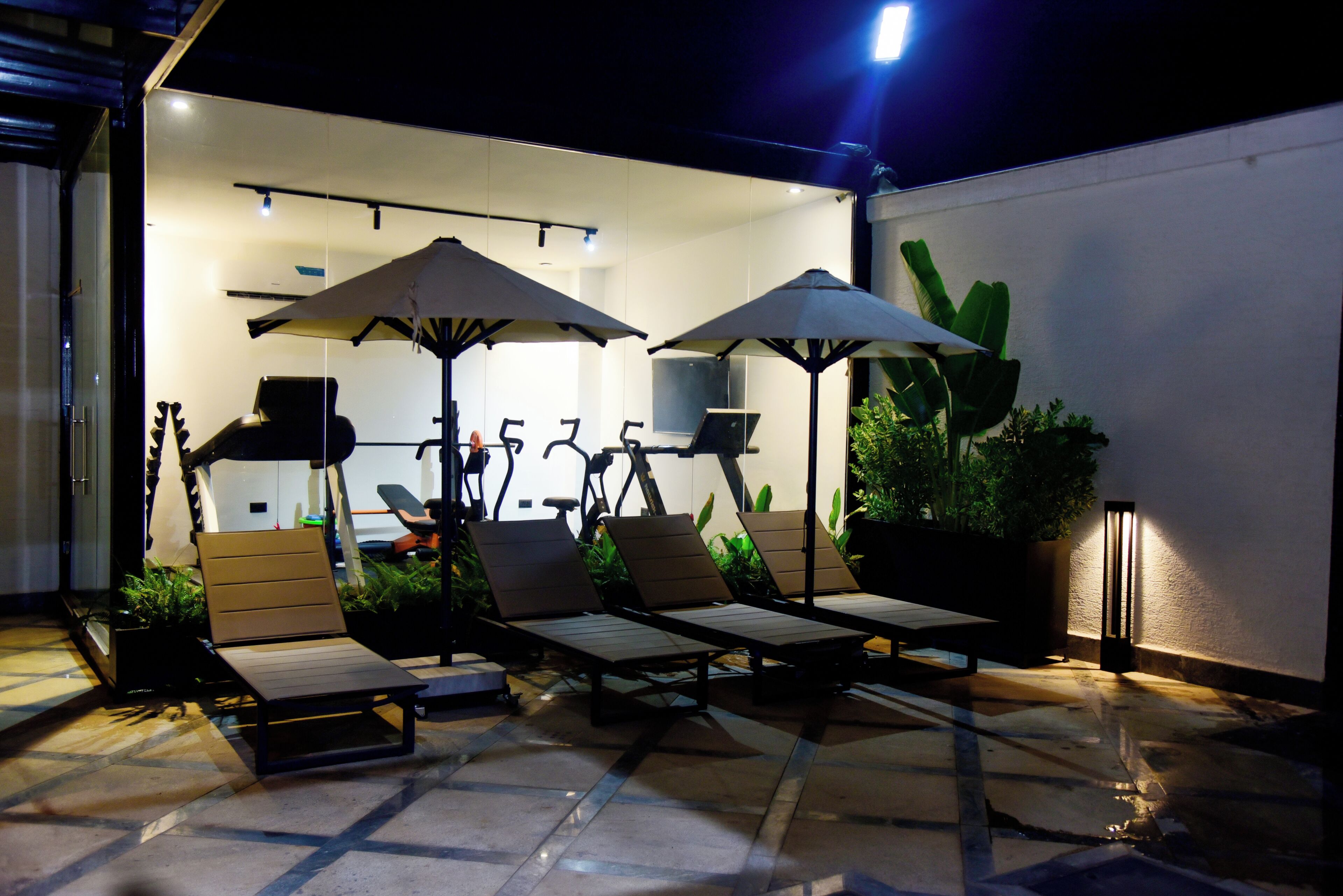Un espace patio aménagé avec des fauteuils de jardin, des parasols et un téléviseur fixé au mur.