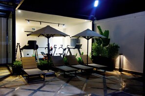 Eine Terrasse mit Liegestühlen, Sonnenschirmen und einem an der Wand befestigten Fernseher.
