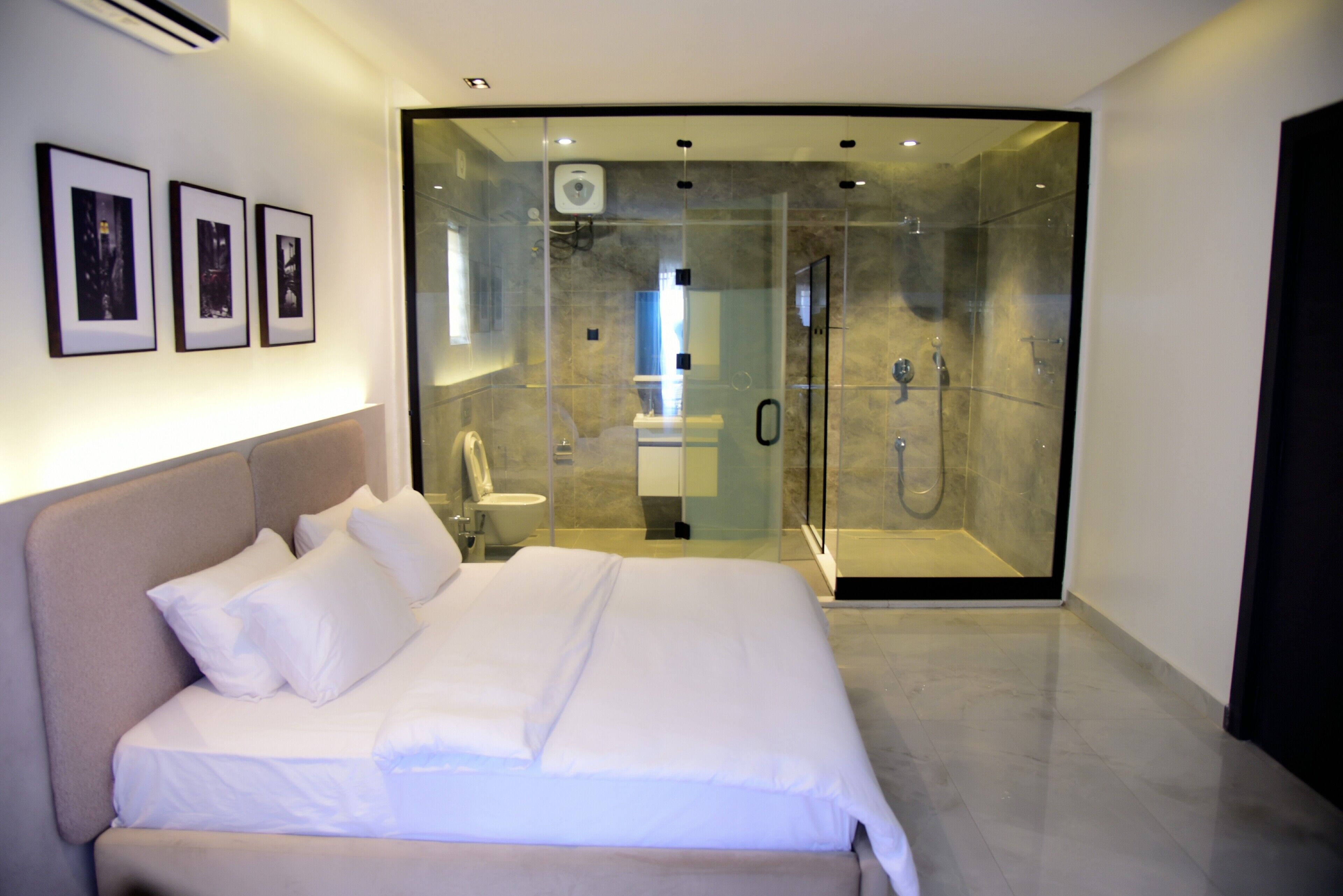 Een moderne slaapkamer met een groot bed, een douchecabine met glazen wanden en ingelijste foto's aan de muur.