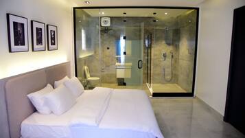 Een moderne slaapkamer met een groot bed, een douchecabine met glazen wanden en ingelijste foto's aan de muur.