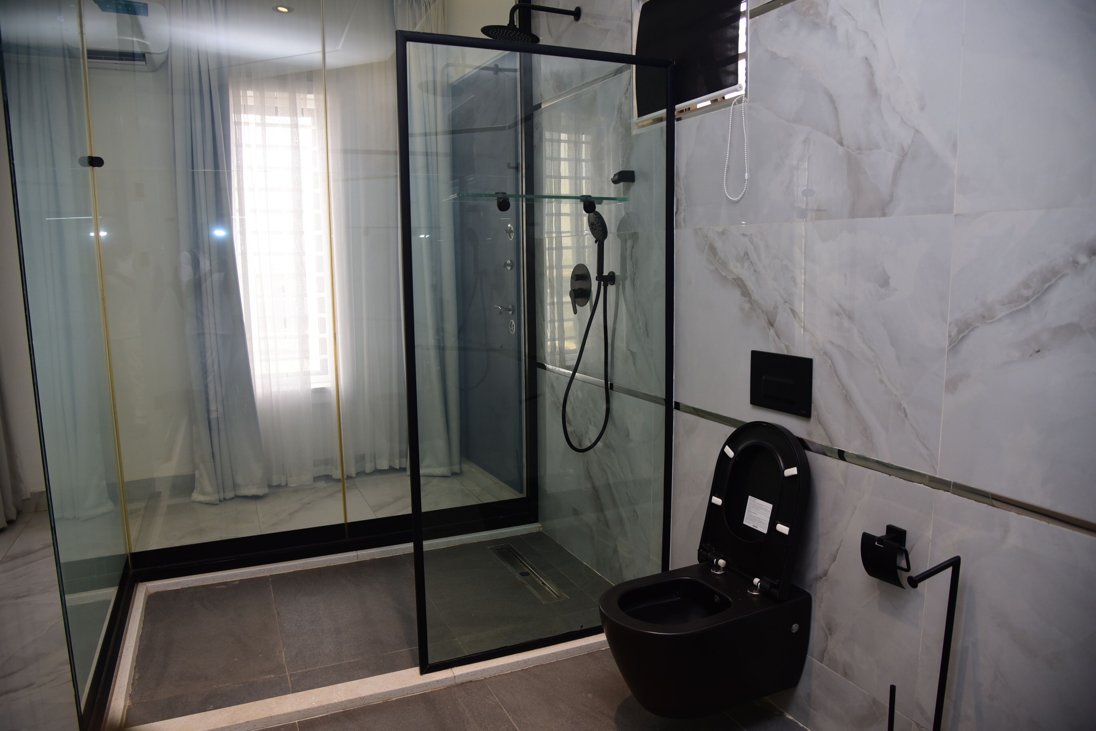A modern bathroom with a glass-enclosed shower, a black toilet, and marble walls.