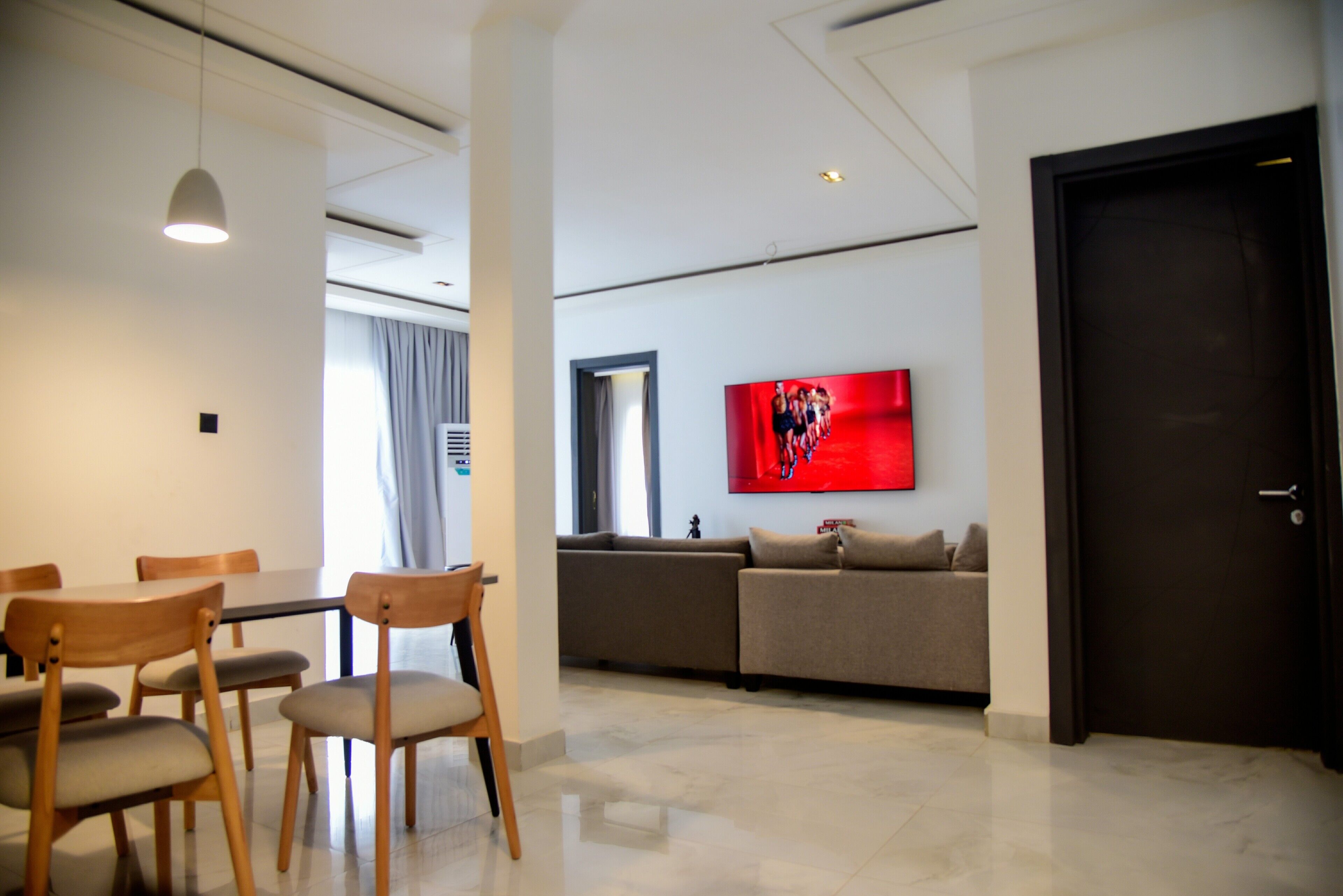 A modern living room with a dining area, a sofa, and a TV mounted on the wall.