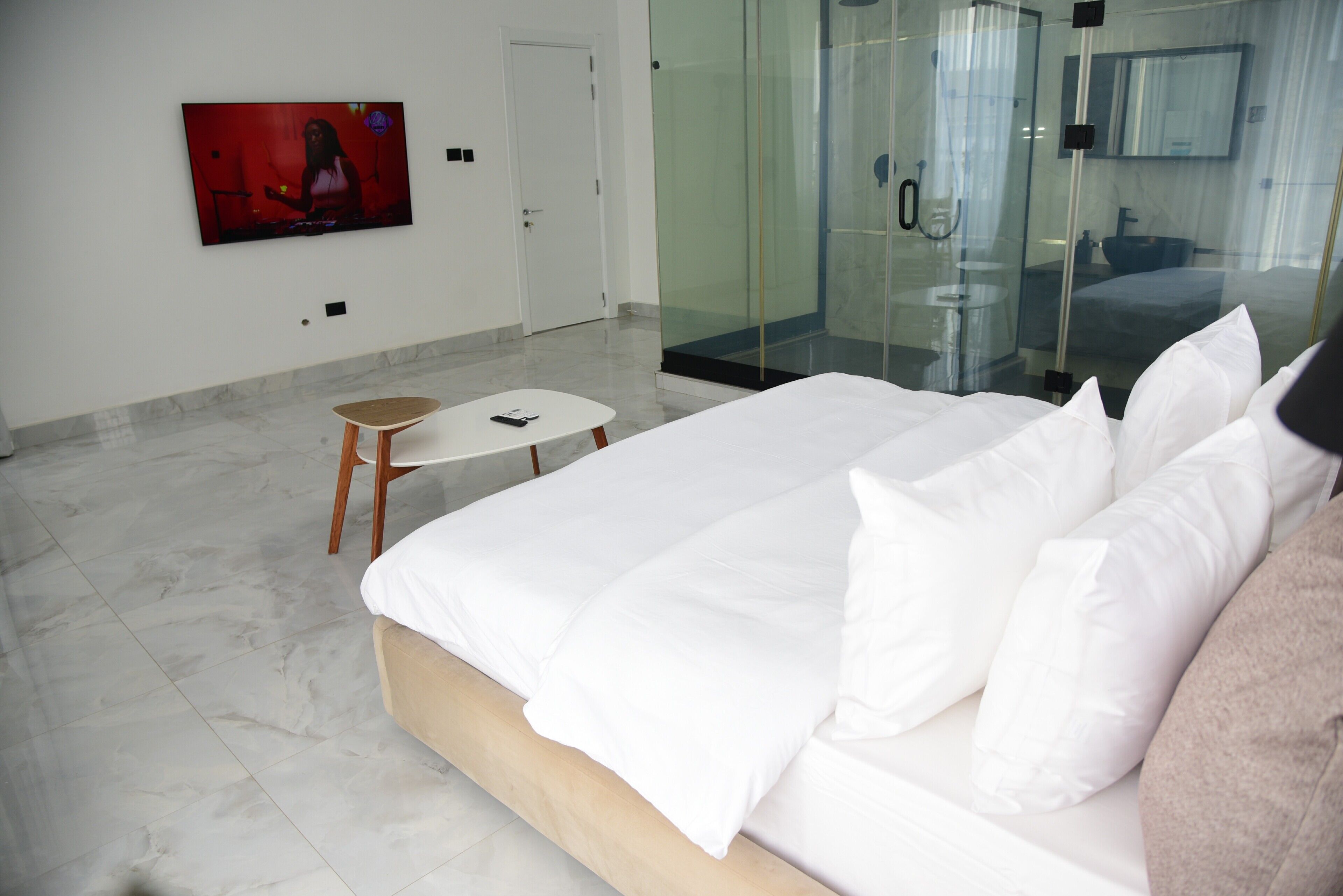 Ein modernes Hotelzimmer mit einem großen Bett, einem kleinen Tisch, einem Fernseher und einer Duschkabine aus Glas.