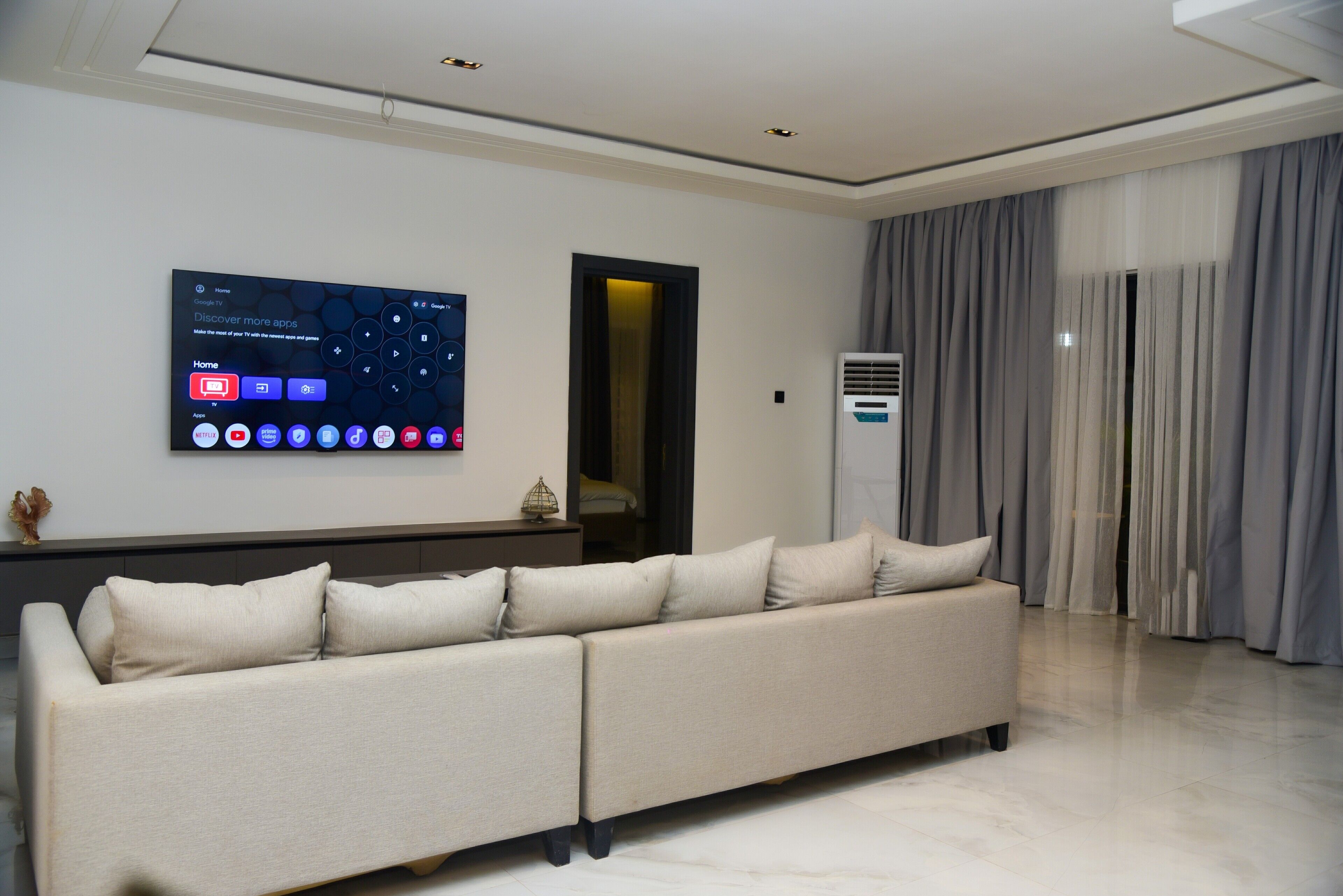 Una sala de estar moderna con un sofá seccional, un televisor de pantalla plana montado y un gran ventanal con cortinas.