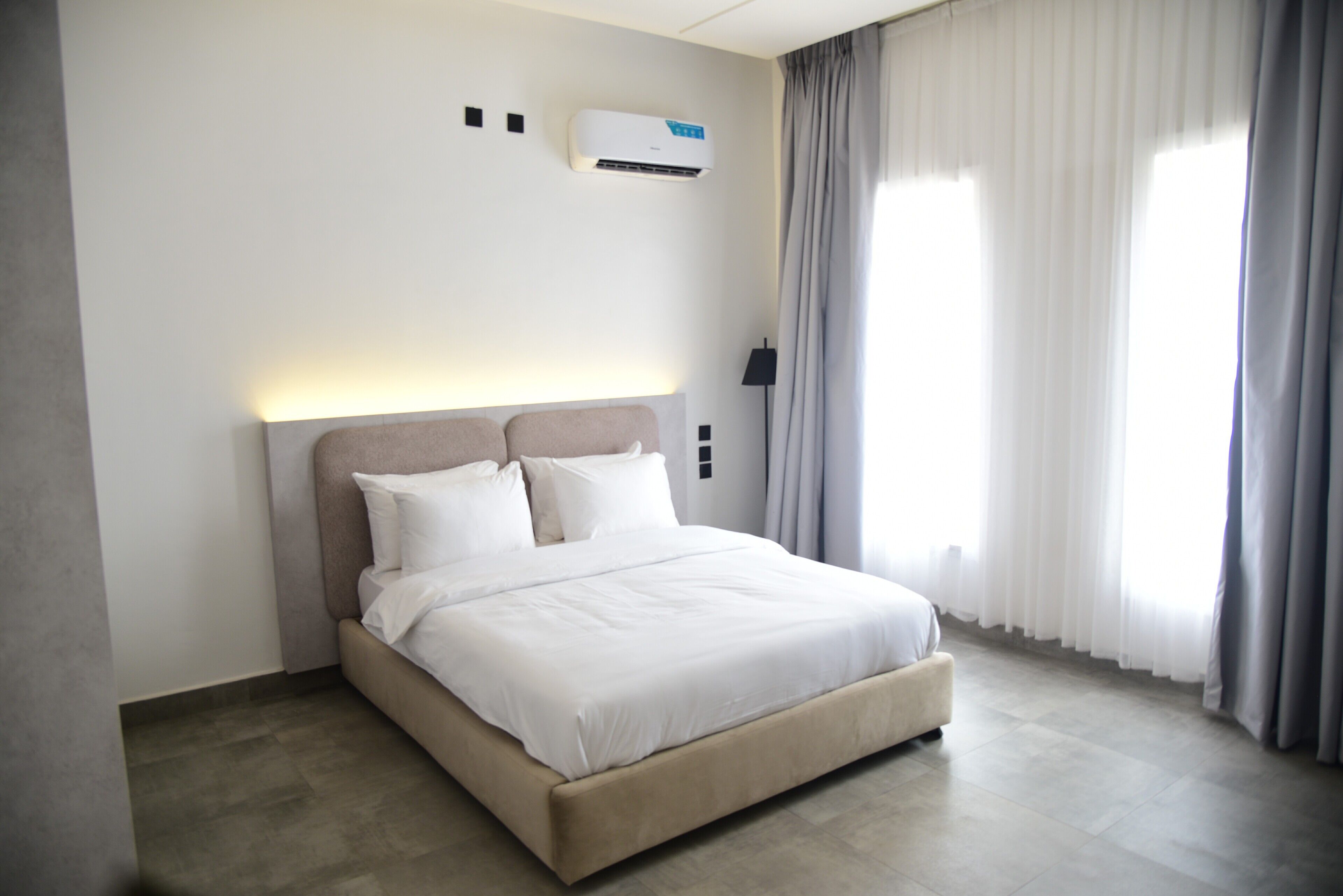 A modern hotel room with a large bed, a wall-mounted air conditioner, and a window with curtains.