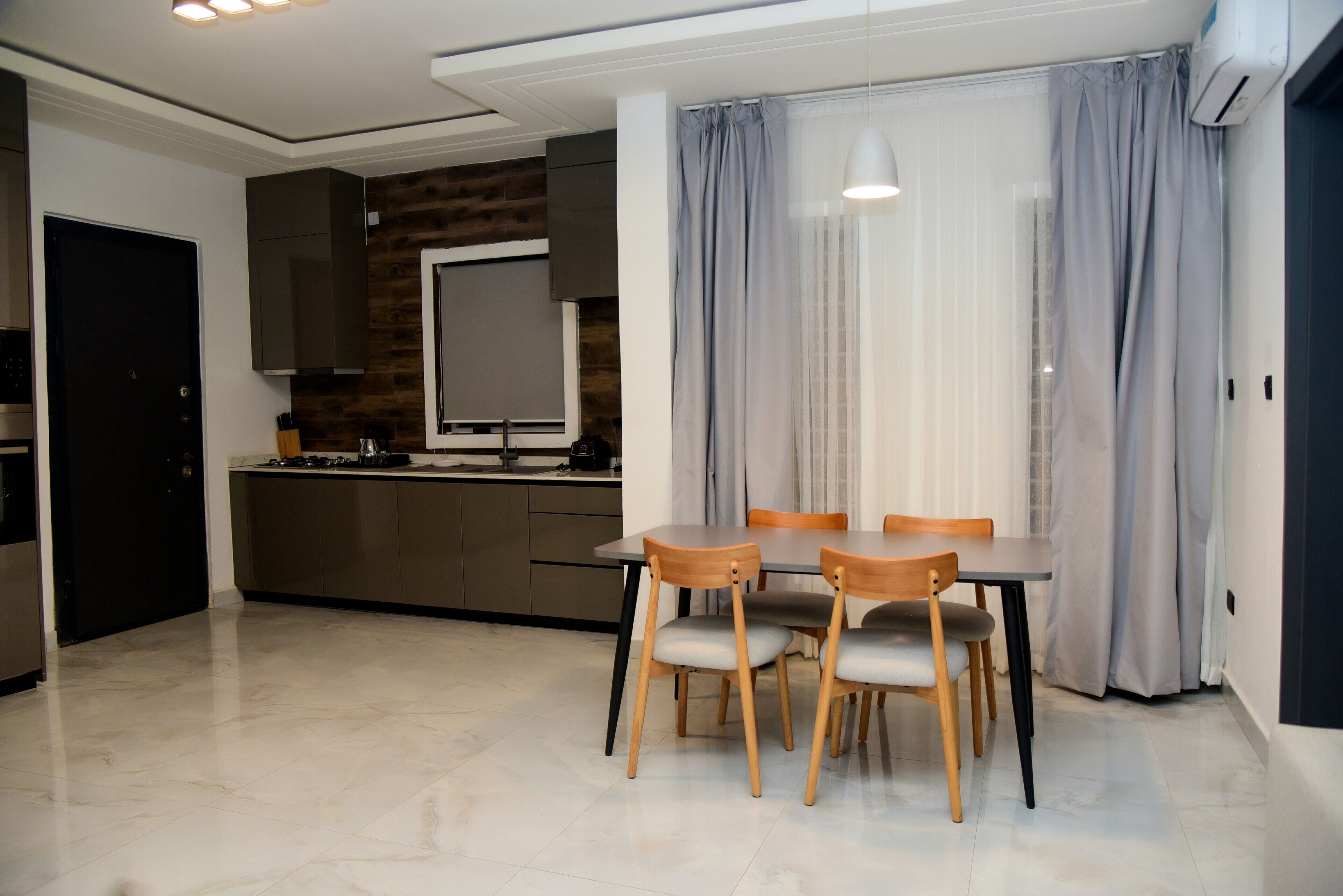 Una cocina moderna con una pared de acento en madera oscura, un área de comedor con una mesa y sillas, y un ventanal con cortinas.