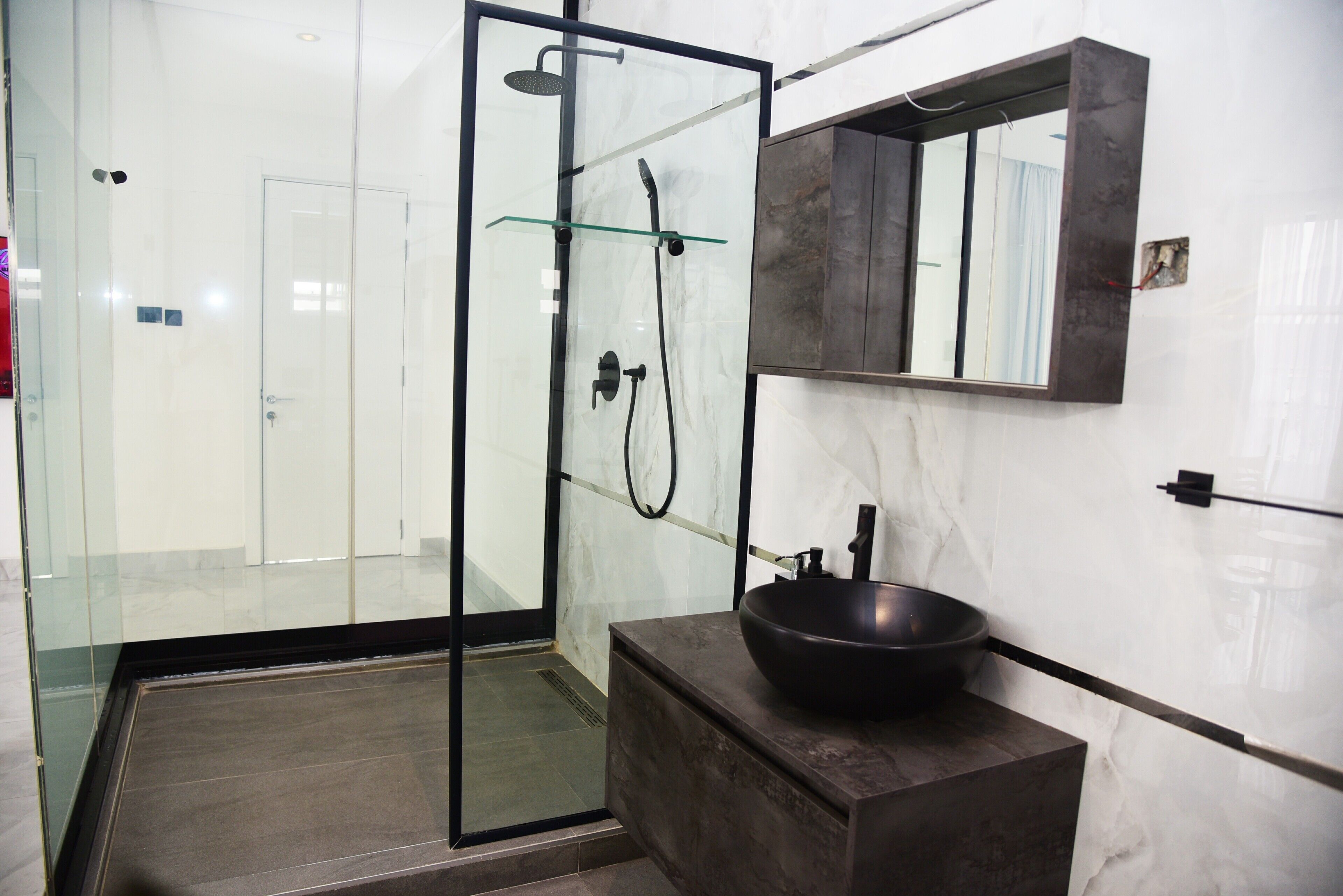 Een moderne badkamer met een douche met glazen wand, een donker aanrecht en een marmeren wand.