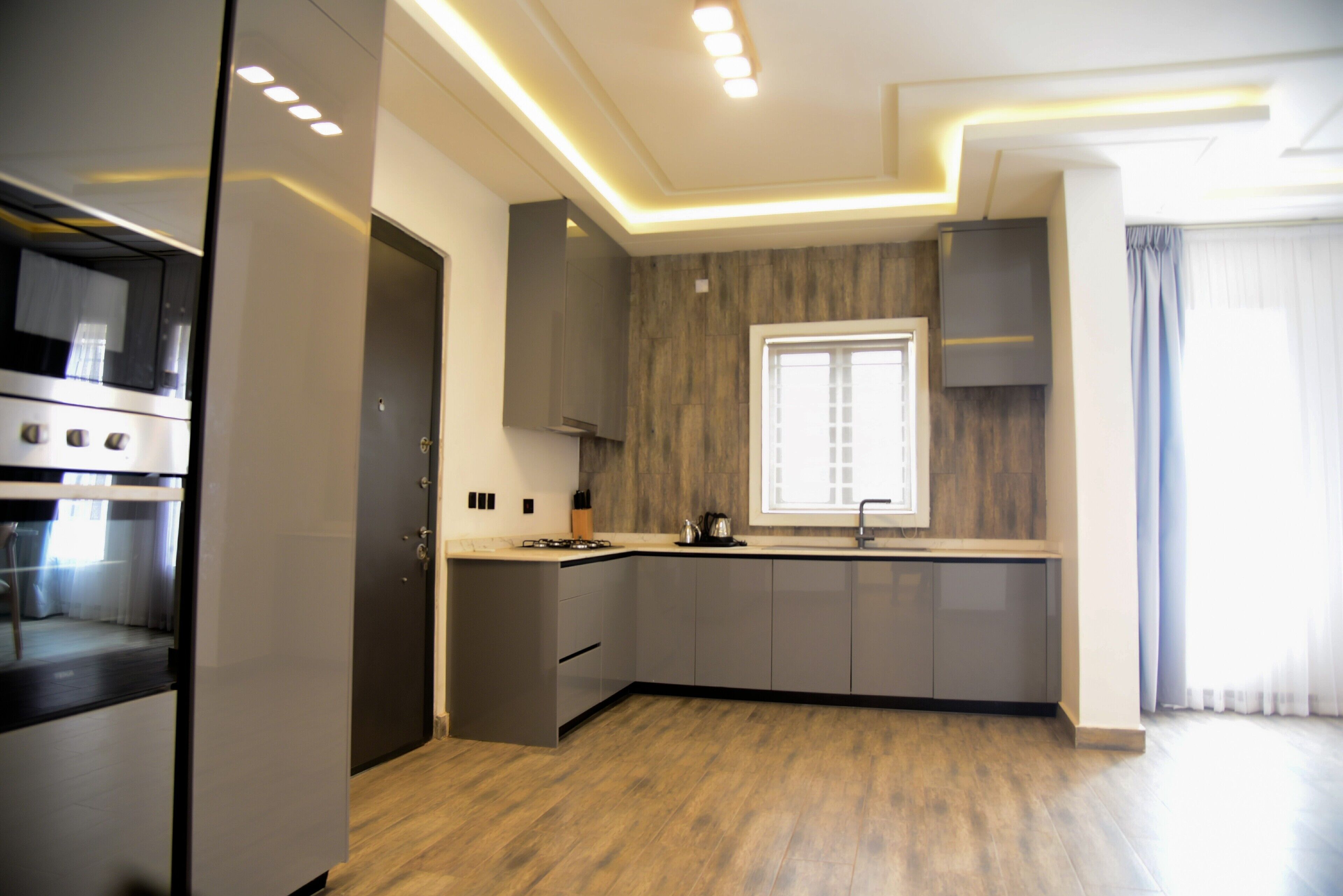 Una cocina moderna con electrodomésticos integrados, armarios grises y un ventanal con cortinas.