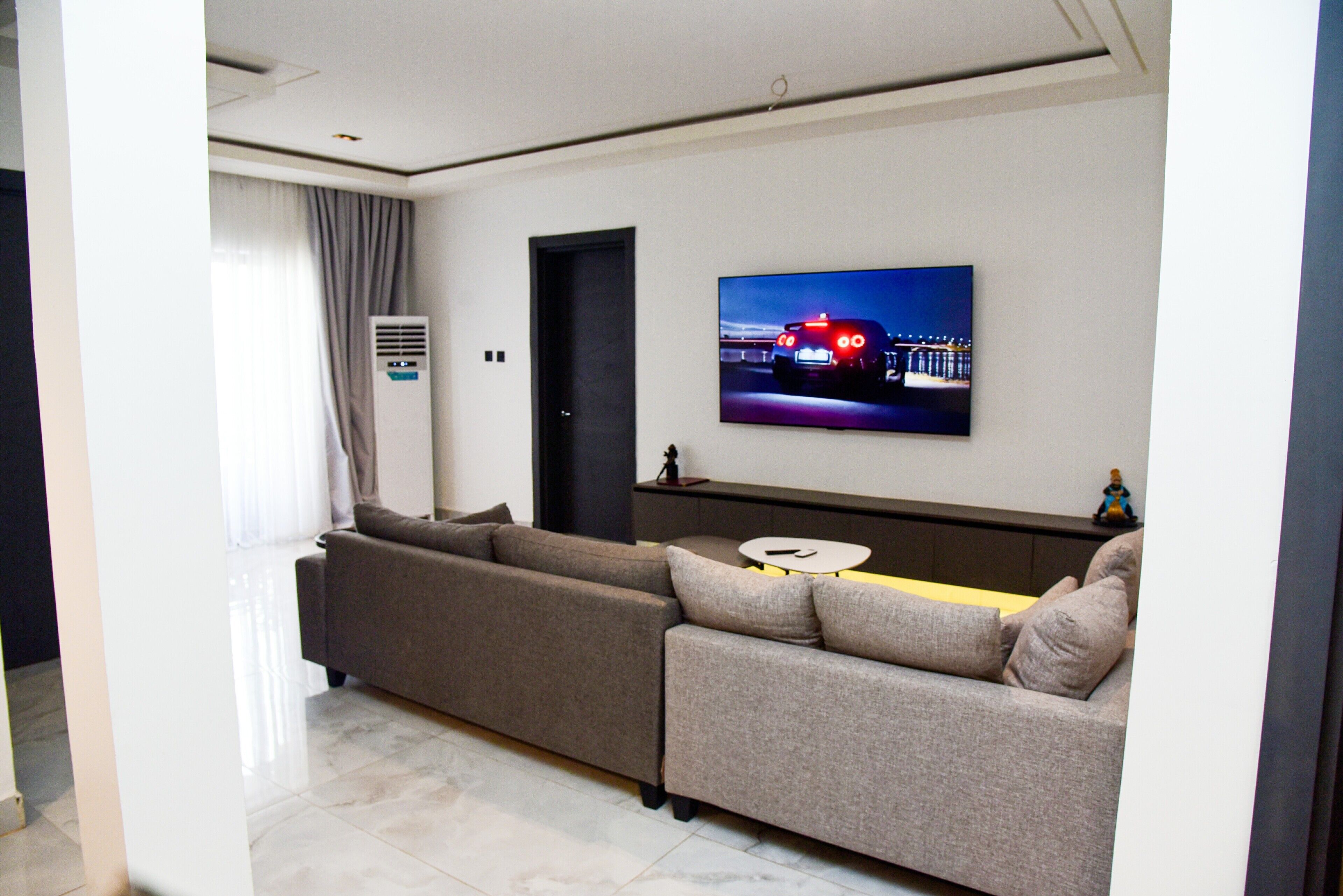A modern living room with a sectional sofa, a flat-screen TV mounted on the wall, and a small round table.