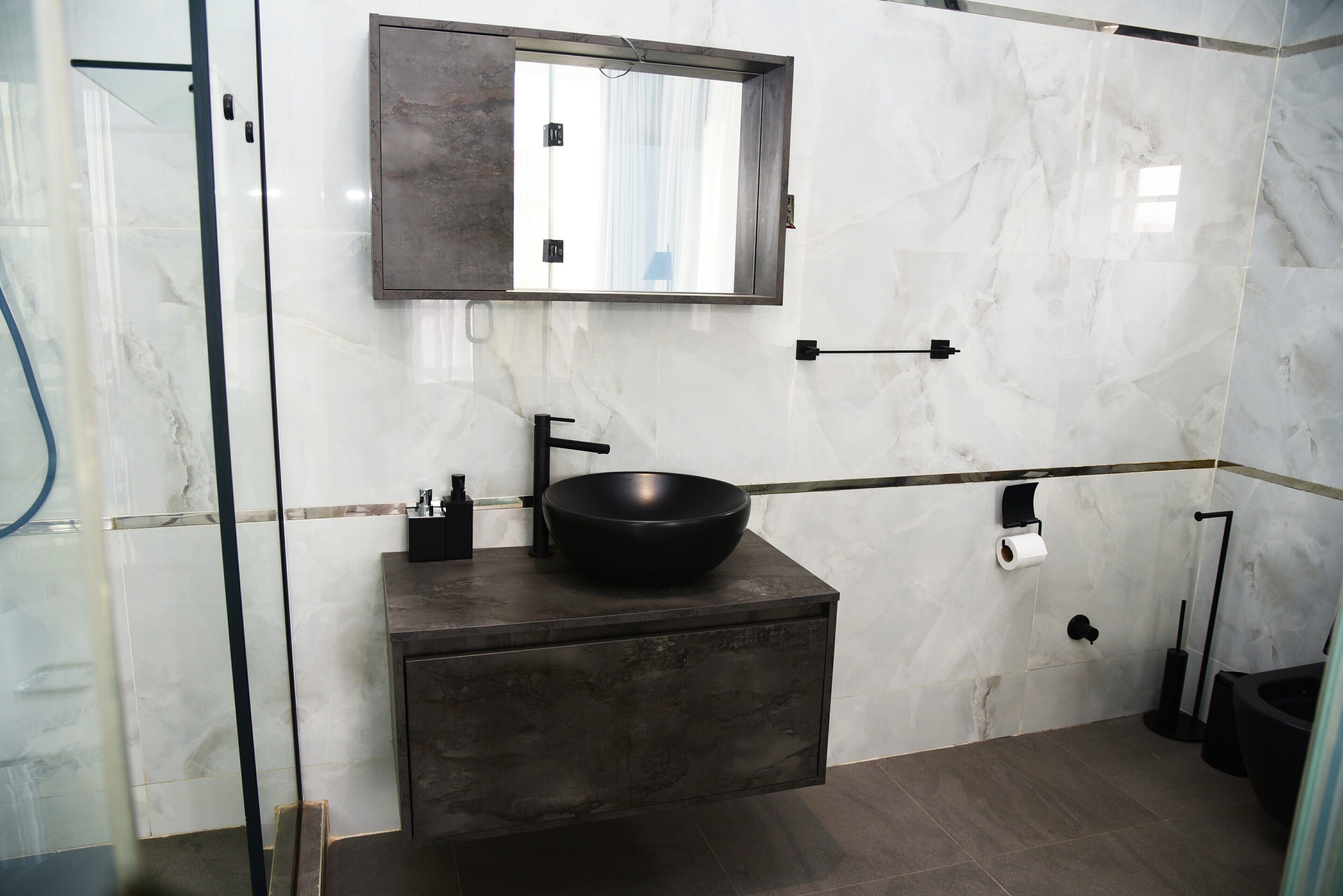 Une salle de bain avec un lavabo noir sur pied, un miroir au-dessus et une cabine de douche en verre.