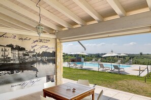 Habitación con un amplio ventanal que da a una piscina y vistas de un pueblo histórico.