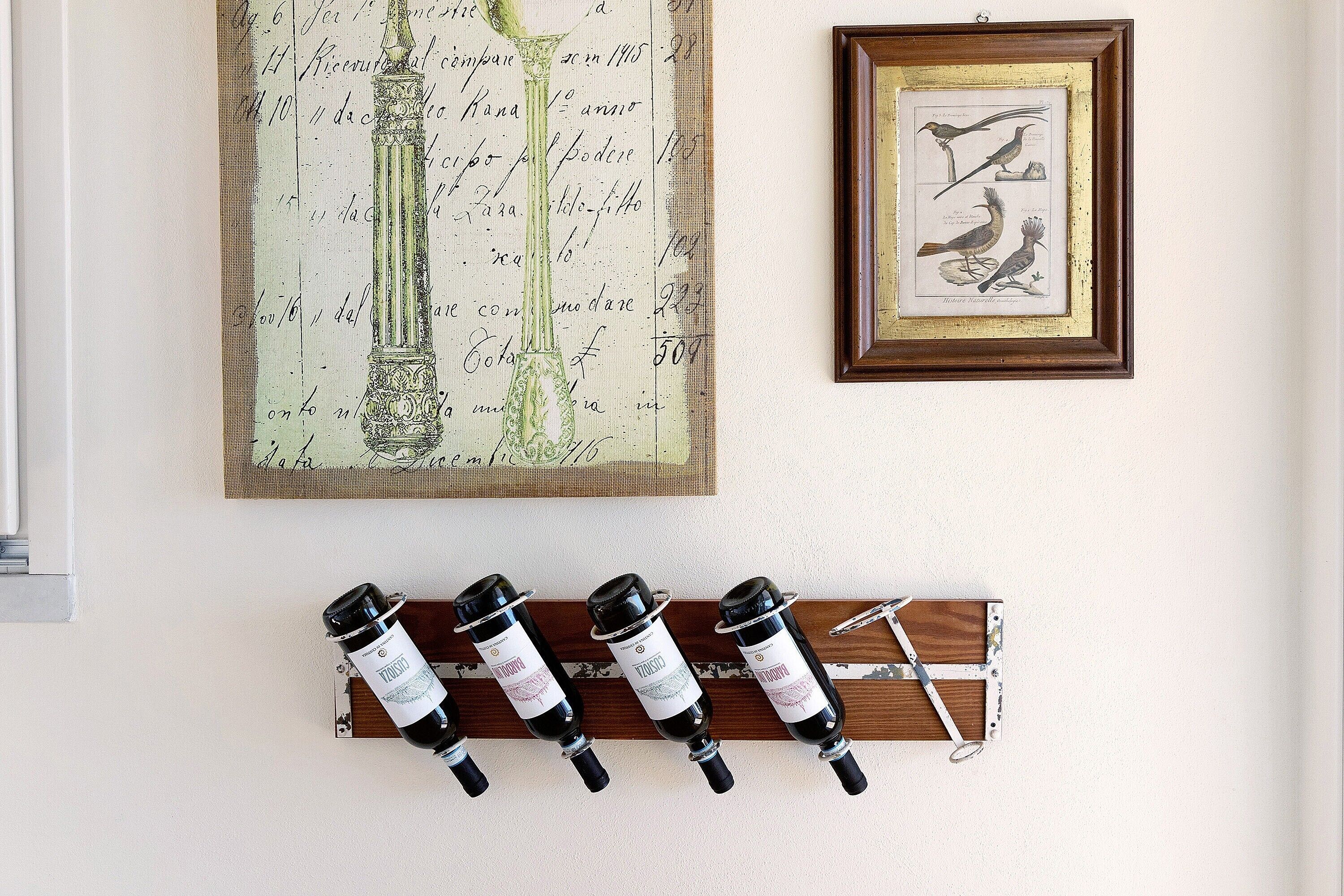 A wall with a framed bird illustration, a large botanical illustration, and a wine rack with bottles.