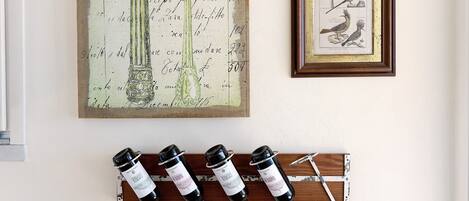 A wall with a framed bird illustration, a large botanical illustration, and a wine rack with bottles.