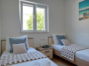 Ein Doppelzimmer mit zwei Betten, einem Fenster mit Blick auf Grünflächen, einem Bild an der Wand und einem Nachttisch mit Telefon.