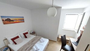 A hotel room with a bed, bedside table, lamp, desk with chair, and a window. - A1 - Chic One-Bedroom Apartment with Parking and Garden view (Slano)