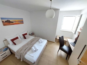 A hotel room with a bed, bedside table, lamp, desk with chair, and a window. - A1 - Chic One-Bedroom Apartment with Parking and Garden view (Slano)