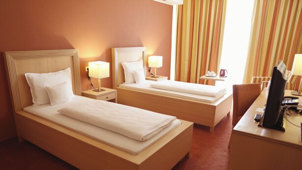 Habitación de hotel con dos camas individuales, mesitas de noche con lámparas, un escritorio con computadora y una ventana con cortinas.