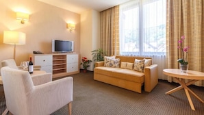Habitación de hotel con sofá, sillón, televisión y una pequeña mesa.