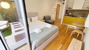 A hotel room with a bed, a chair, a small desk, a kitchen area, and a view through a glass door. - Studio apartment with patio in Câmara de Lobos | Privileged location (Câmara de Lobos)