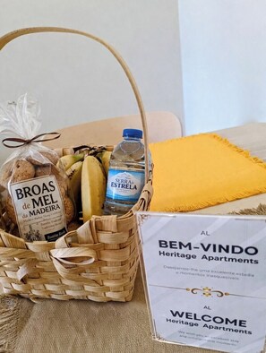 A welcome sign for Heritage Apartments, a wicker basket with bread, bananas, and a water bottle. - Studio apartment with patio in Câmara de Lobos | Privileged location (Câmara de Lobos)