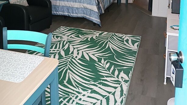 Ett sovrum med en säng, en stol, ett skrivbord, en liten köksdel och en skylt med texten ”STRANDLIV”.