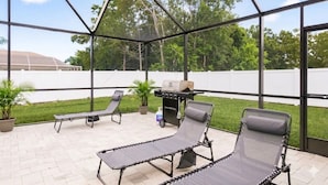 A covered patio area with lounge chairs, a grill, and a view of the surrounding greenery.