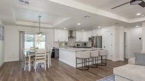 A modern kitchen with a central island, bar stools, and a dining area with chairs.