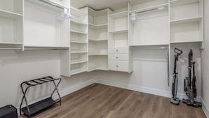 A walk-in closet with open shelving, a bench, and vacuum cleaners.