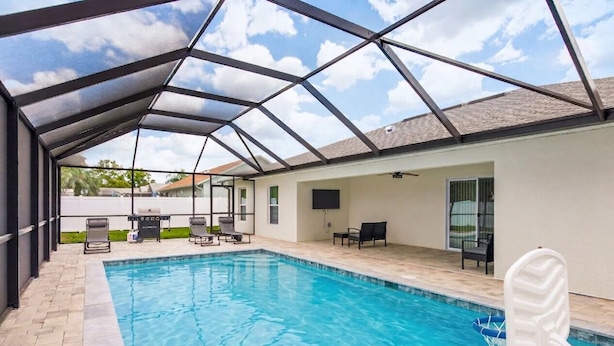 An indoor swimming pool with a glass ceiling, lounge chairs, and a TV.