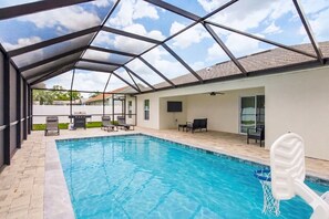 An indoor swimming pool with a glass ceiling, lounge chairs, and a TV.