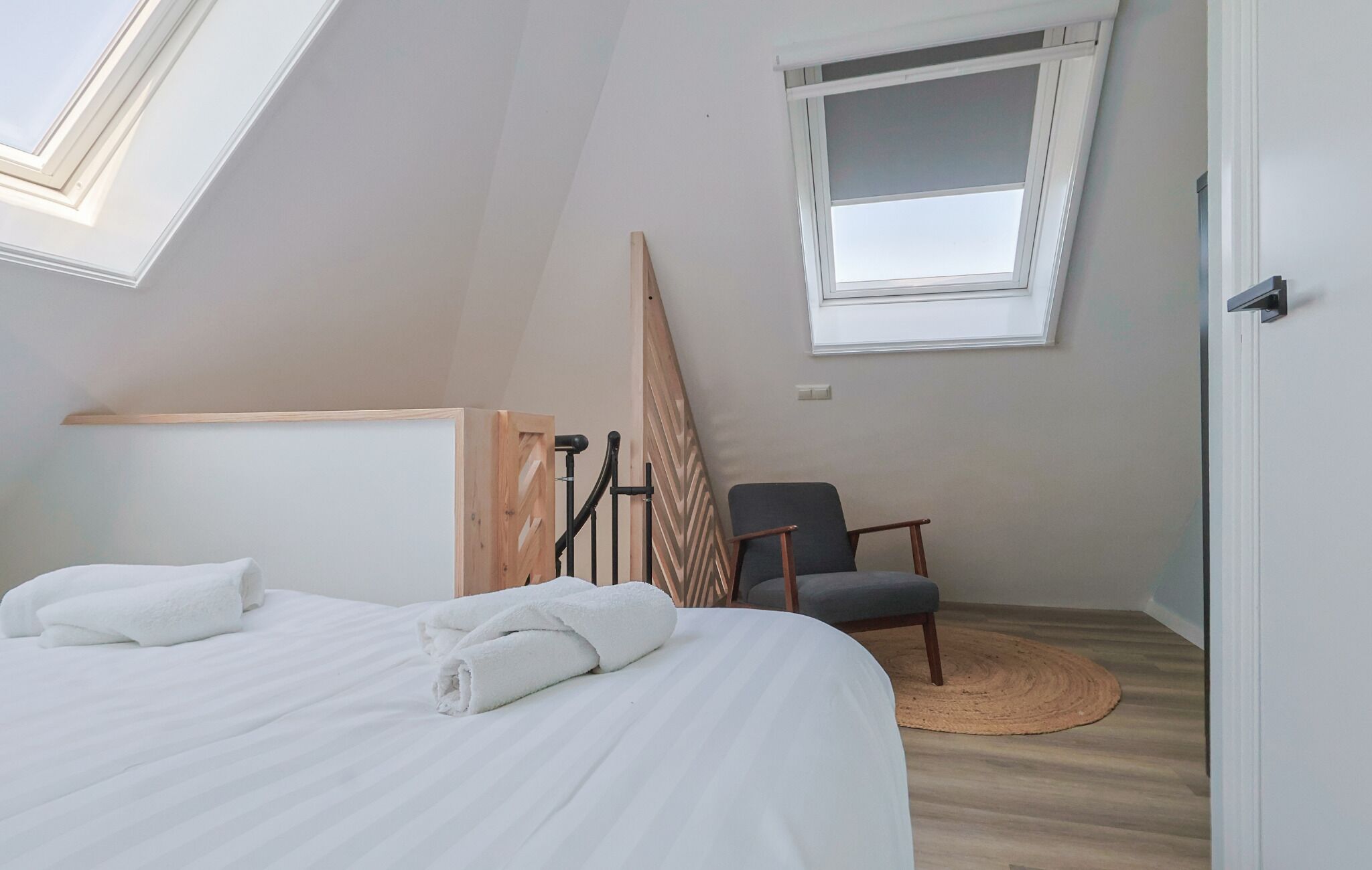 A bedroom with a bed, a chair, a window, and a wooden structure.