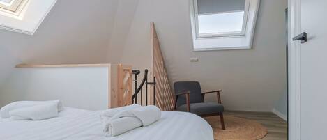 A bedroom with a bed, a chair, a window, and a wooden structure.