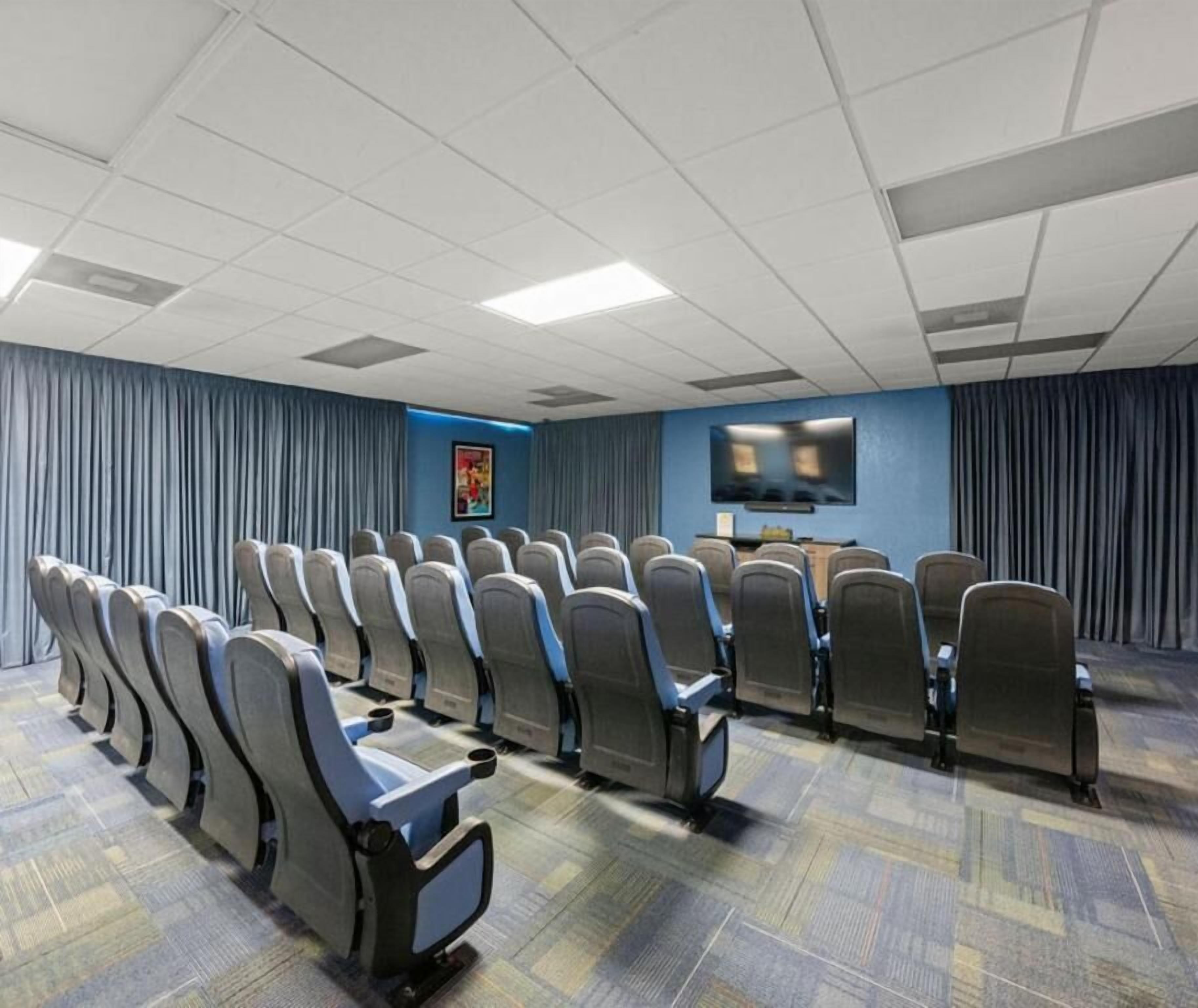 A conference room with rows of chairs, a television screen, and a blue wall with a poster.