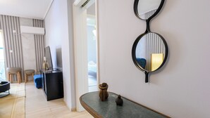 Ein modernes Interieur mit einem gebogenen Holzkonsolentisch, zwei Wandspiegeln, einer kleinen Dekorationsvase und einer Sitzecke mit Stuhl und Hocker.