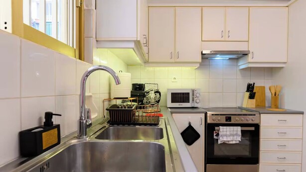 Eine moderne Küche mit Edelstahlspülen, einer Mikrowelle, einem Backofen und weißen Schränken.